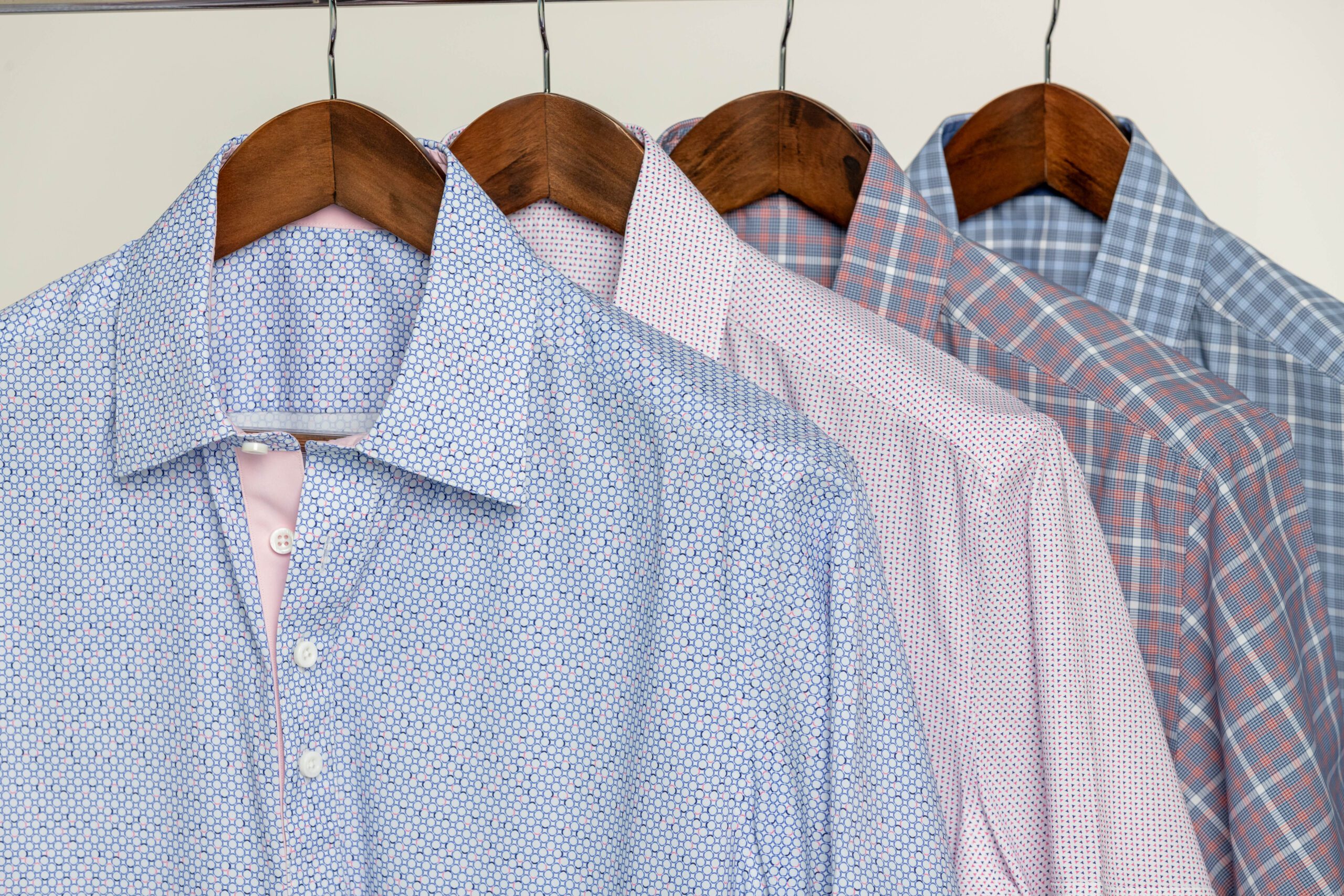 Four shirts hanging neatly on wooden hangers.